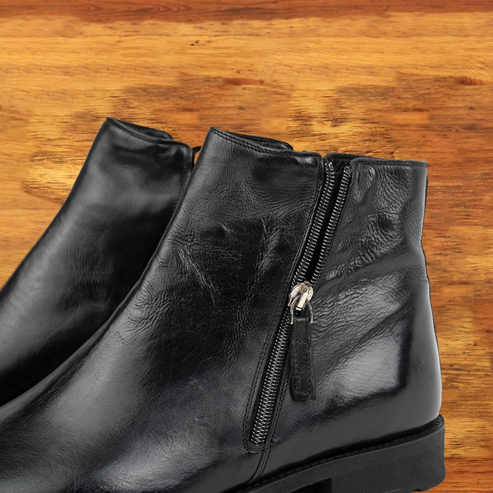 A Pair of Black leather ankle boot with a zipper on a wooden surface