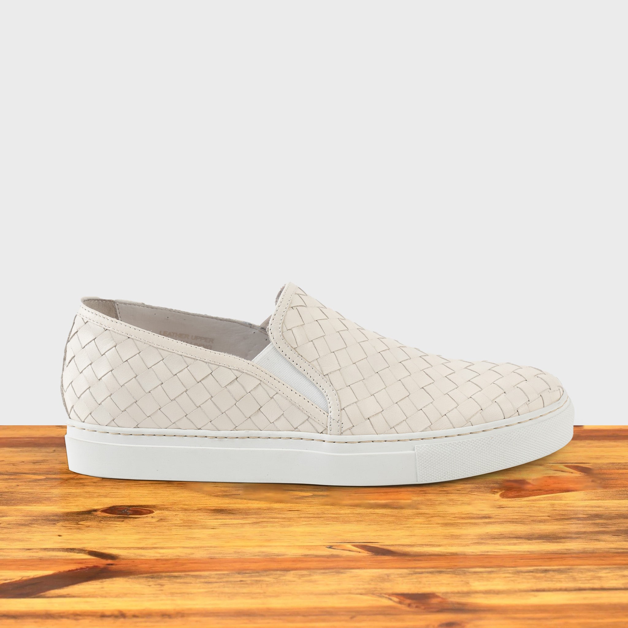 White woven slip-on shoe on a wooden surface with a white background