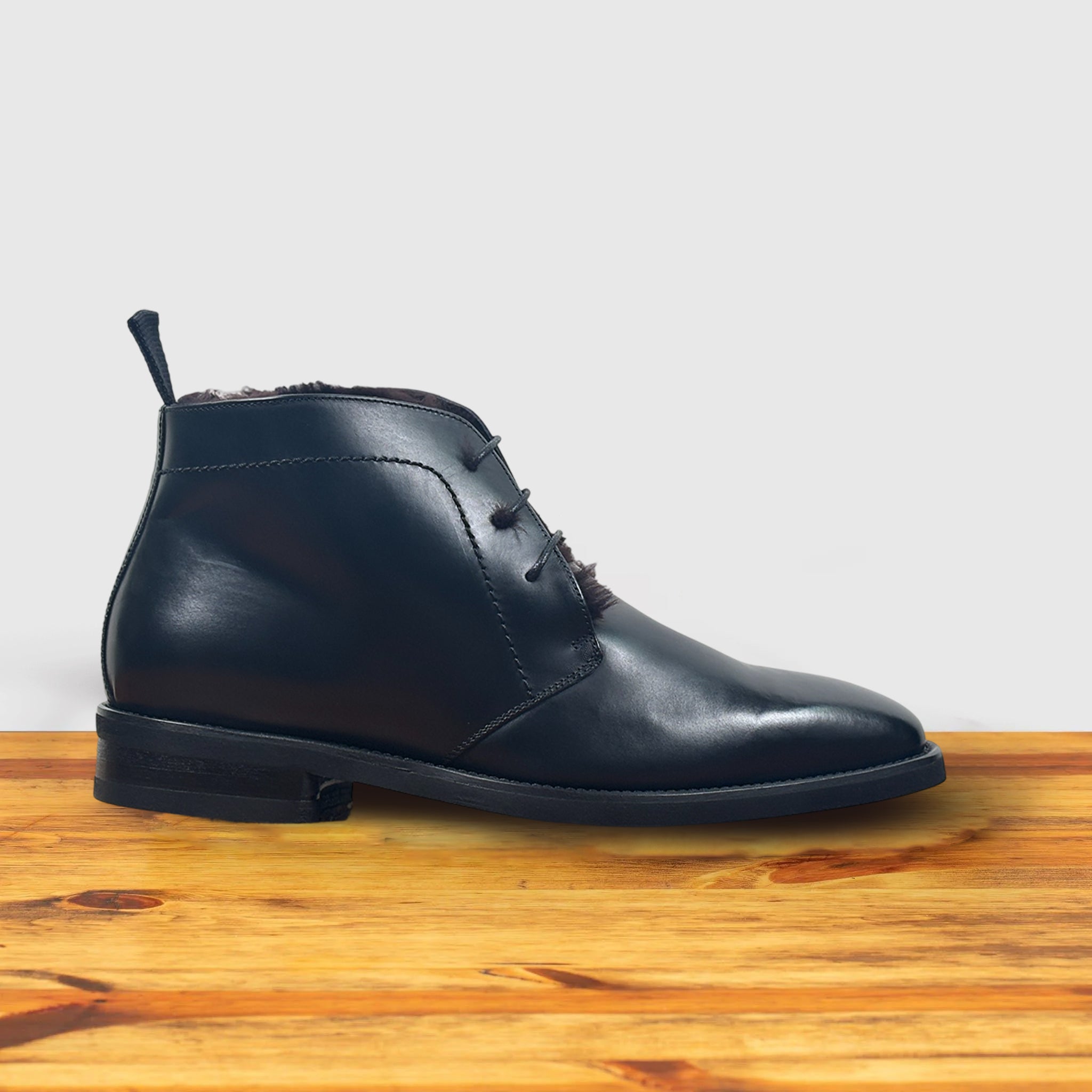 Black leather boot on a wooden surface with a light gray background