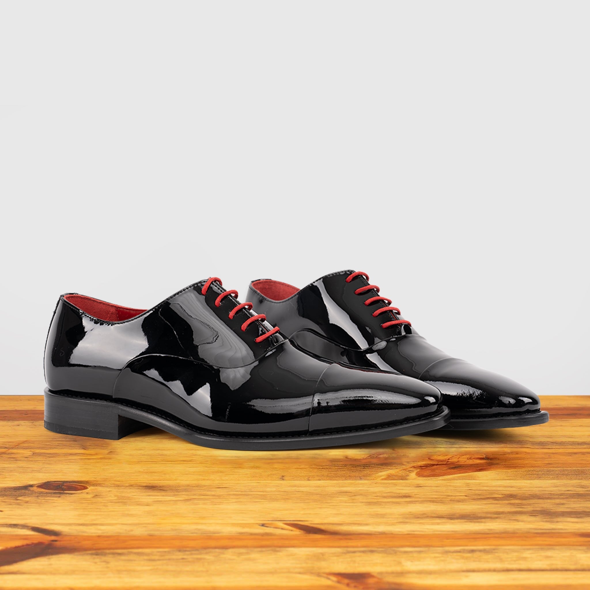 Pair of Black patent leather shoe with red laces on a wooden surface