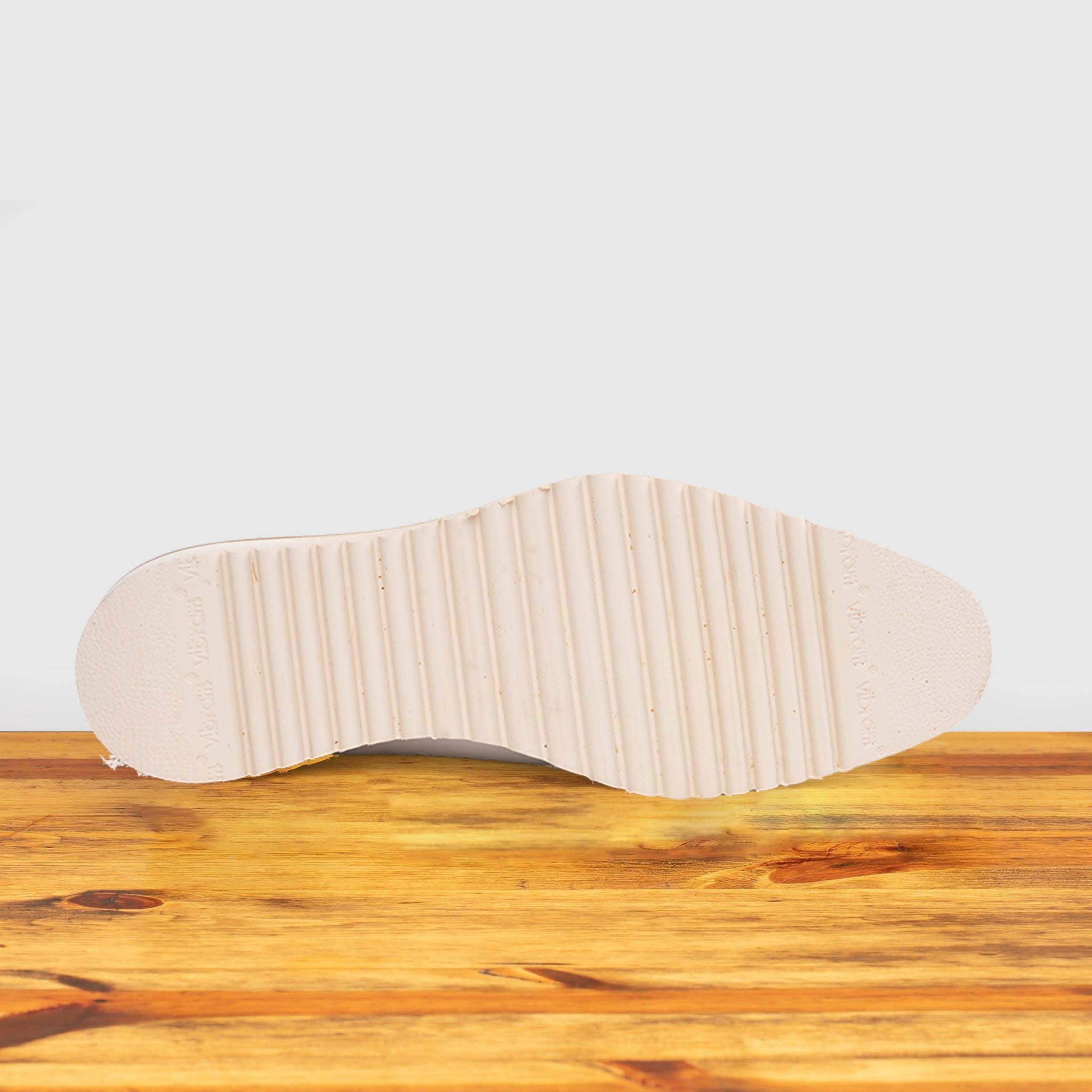 Outsole of White shoe on a wooden surface with a light gray background