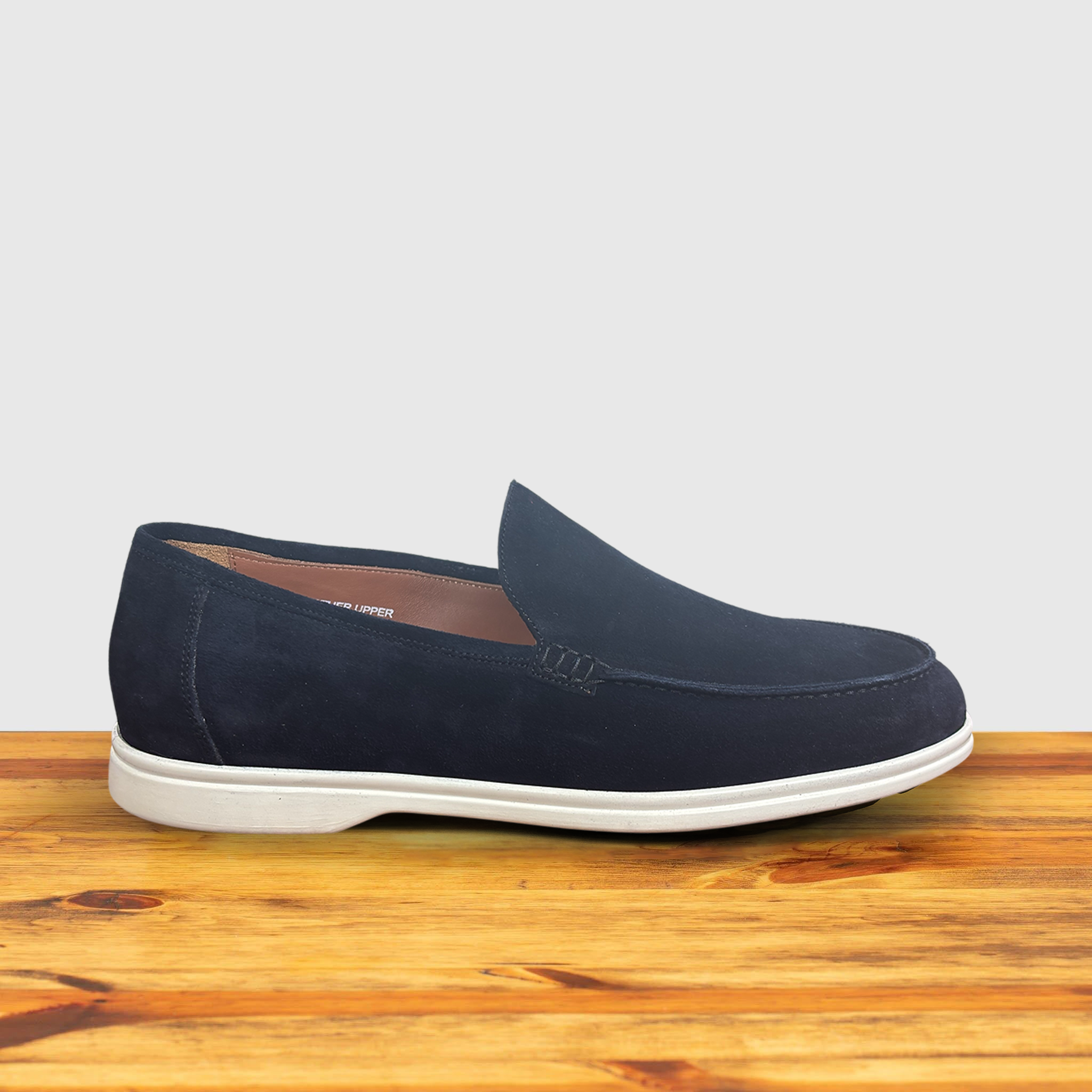 A Navy Blue suede loafer with  white sole, displayed on a wooden surface.
