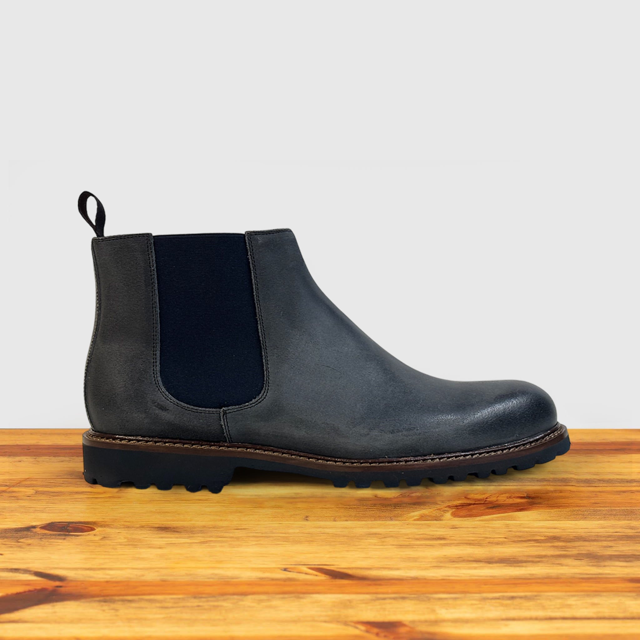 Stone leather Chelsea boots on a wooden surface with a light gray background