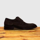 Brown suede dress shoe on a wooden surface with a light gray background