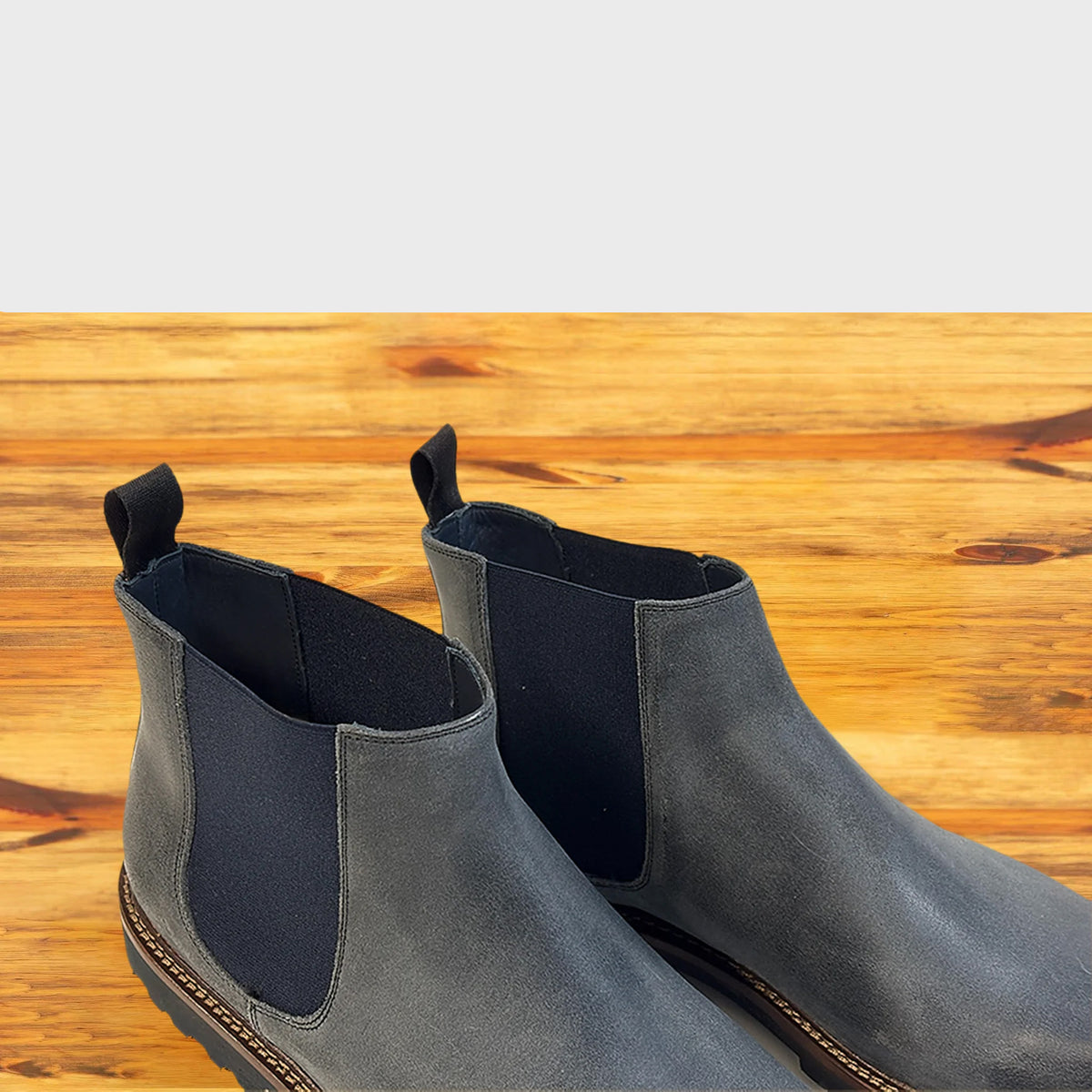 Close view of Stone leather Chelsea boots on a wooden surface