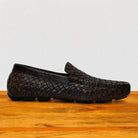 Dark Brown loafer shoe with woven pattern on a wooden surface