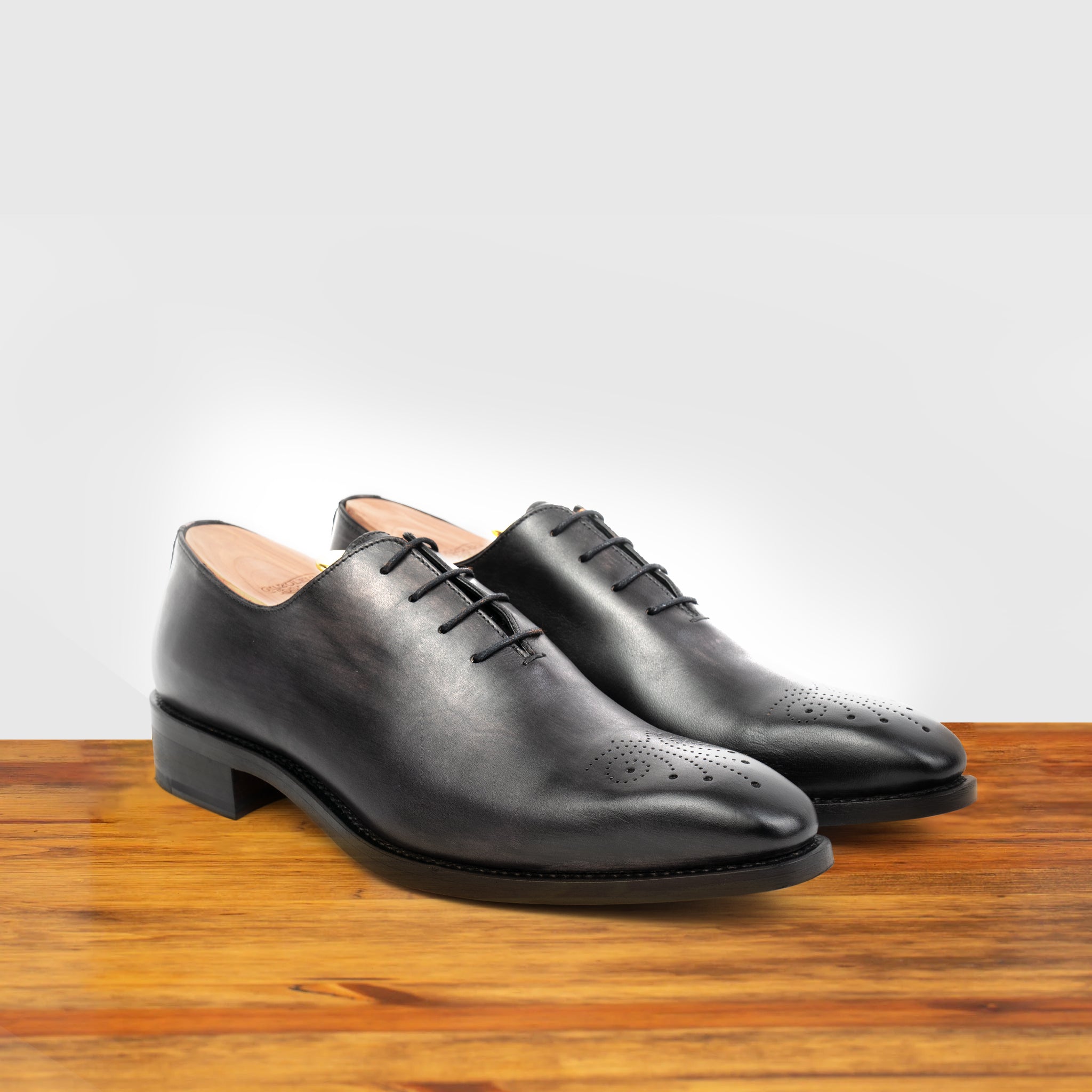 A Pair of Black leather dress shoe on a wooden surface with a gray background
