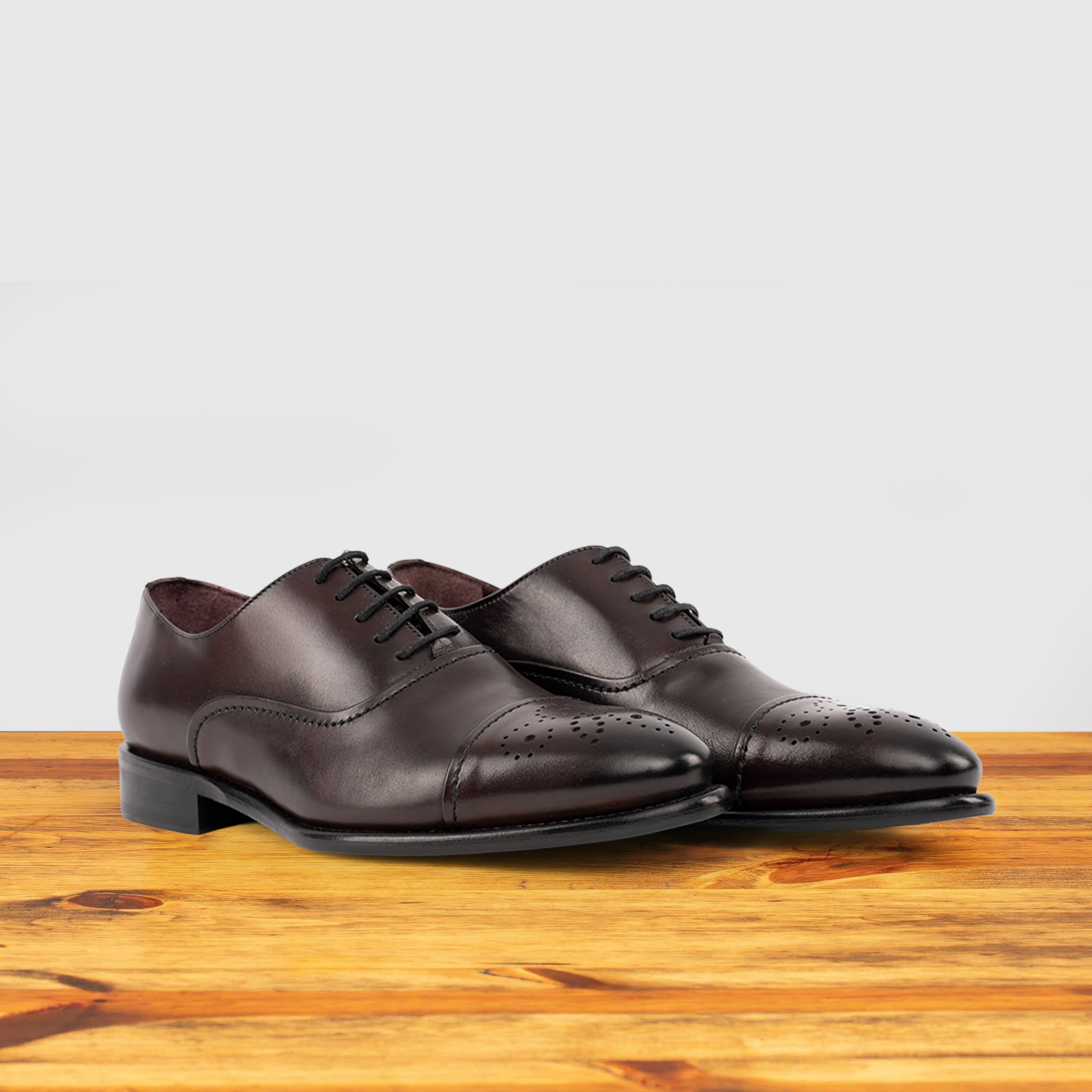 Pair of Burgundy leather dress shoe on a wooden surface with a white background