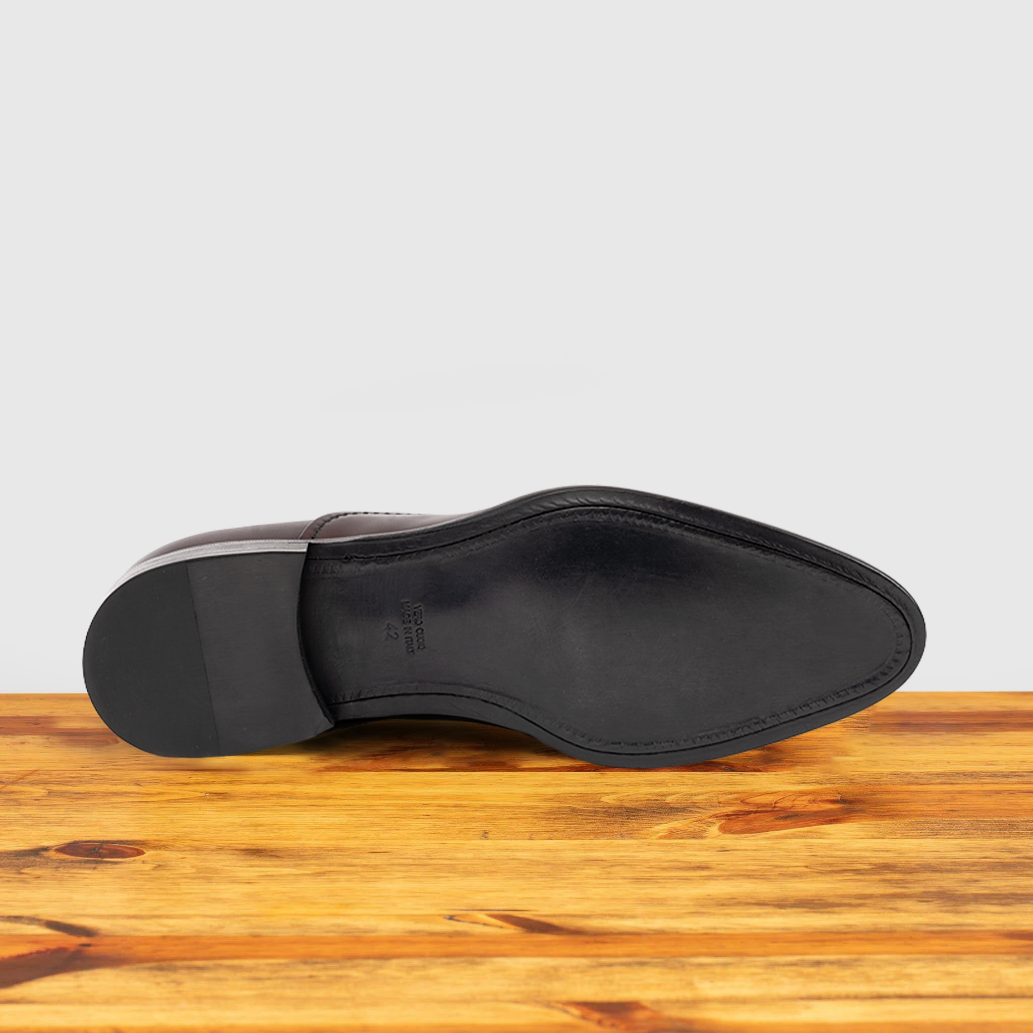 Outsole of Burgundy leather dress shoe on a wooden surface with a white background