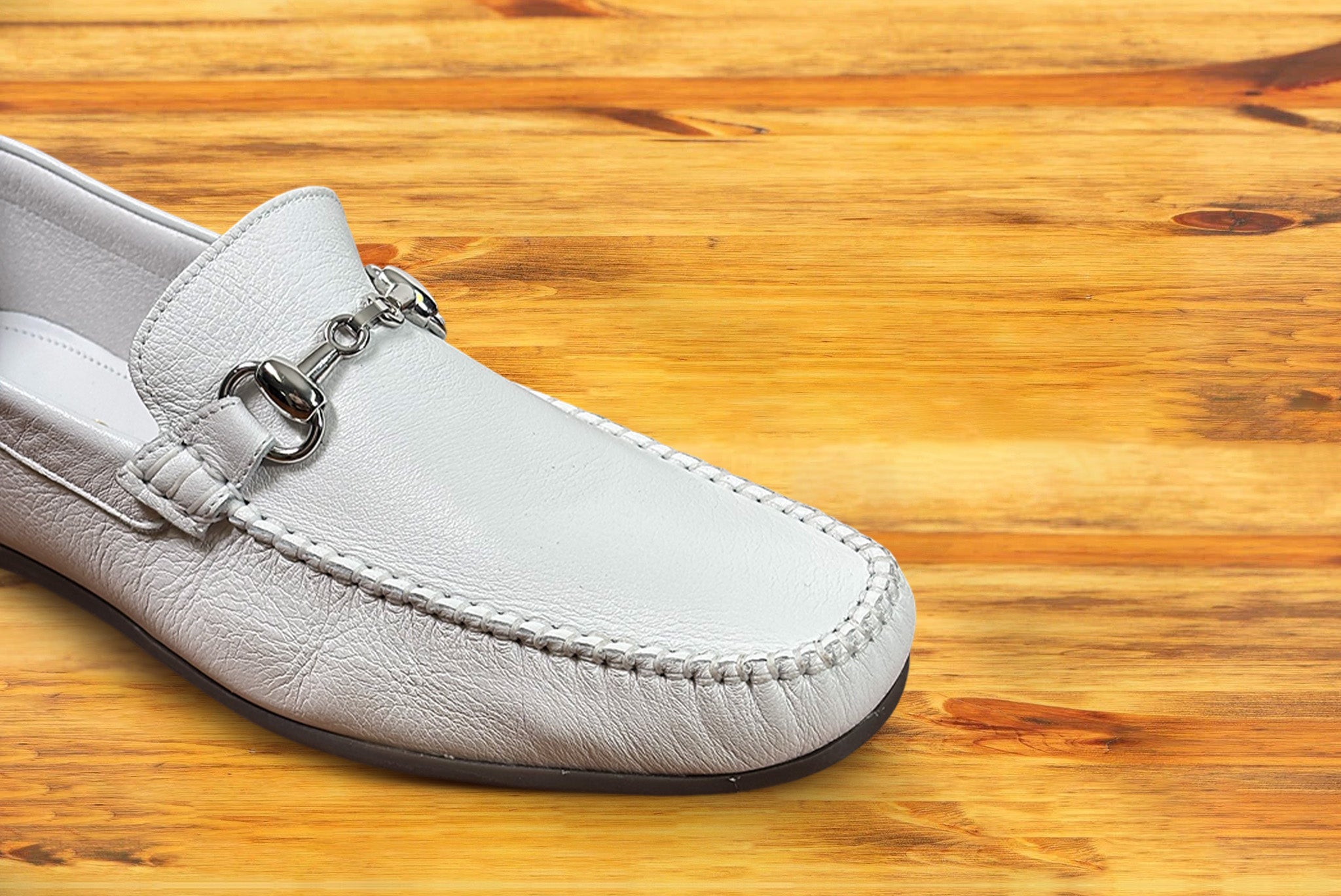 White loafer shoe with silver buckle on a wooden surface