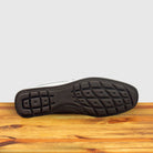 Outsole of White loafer shoe with silver buckle on a wooden surface with a light gray background