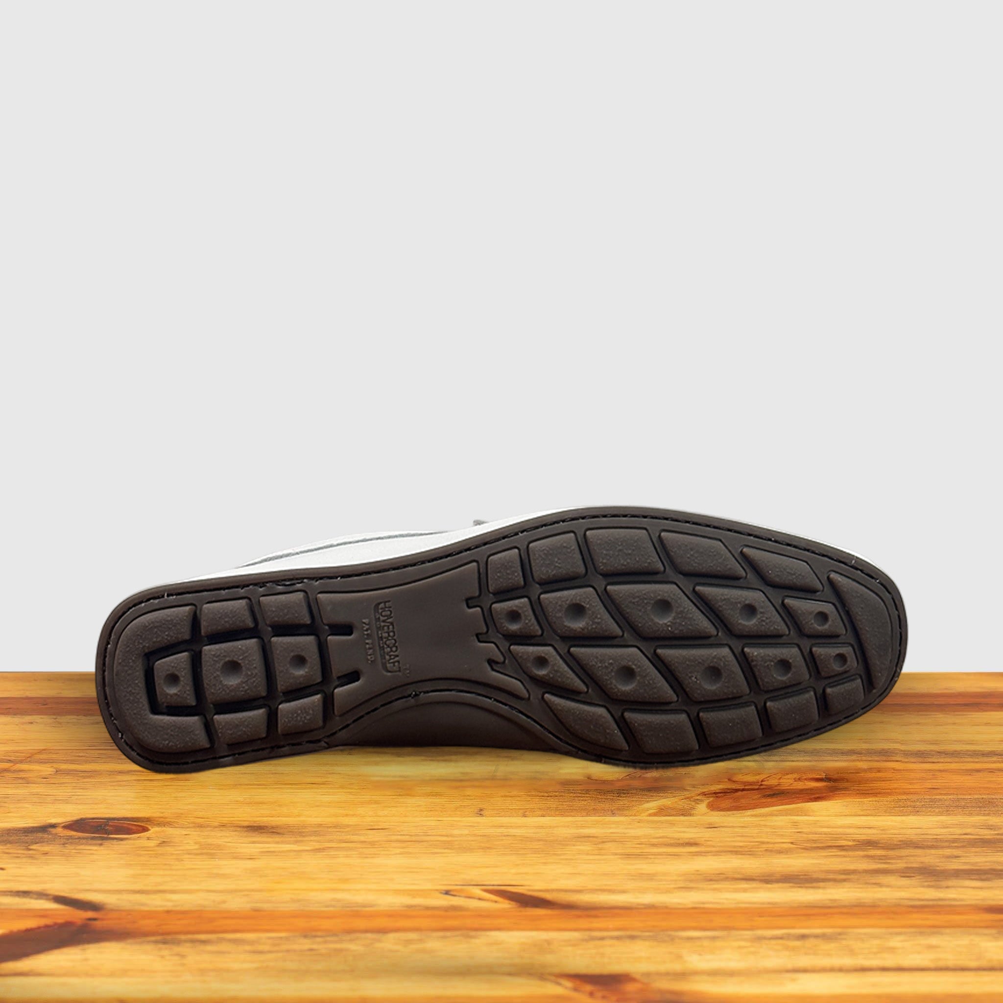 Outsole of White loafer shoe with silver buckle on a wooden surface with a light gray background