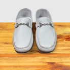 Pair of White loafer shoe with silver buckle on a wooden surface with a light gray background