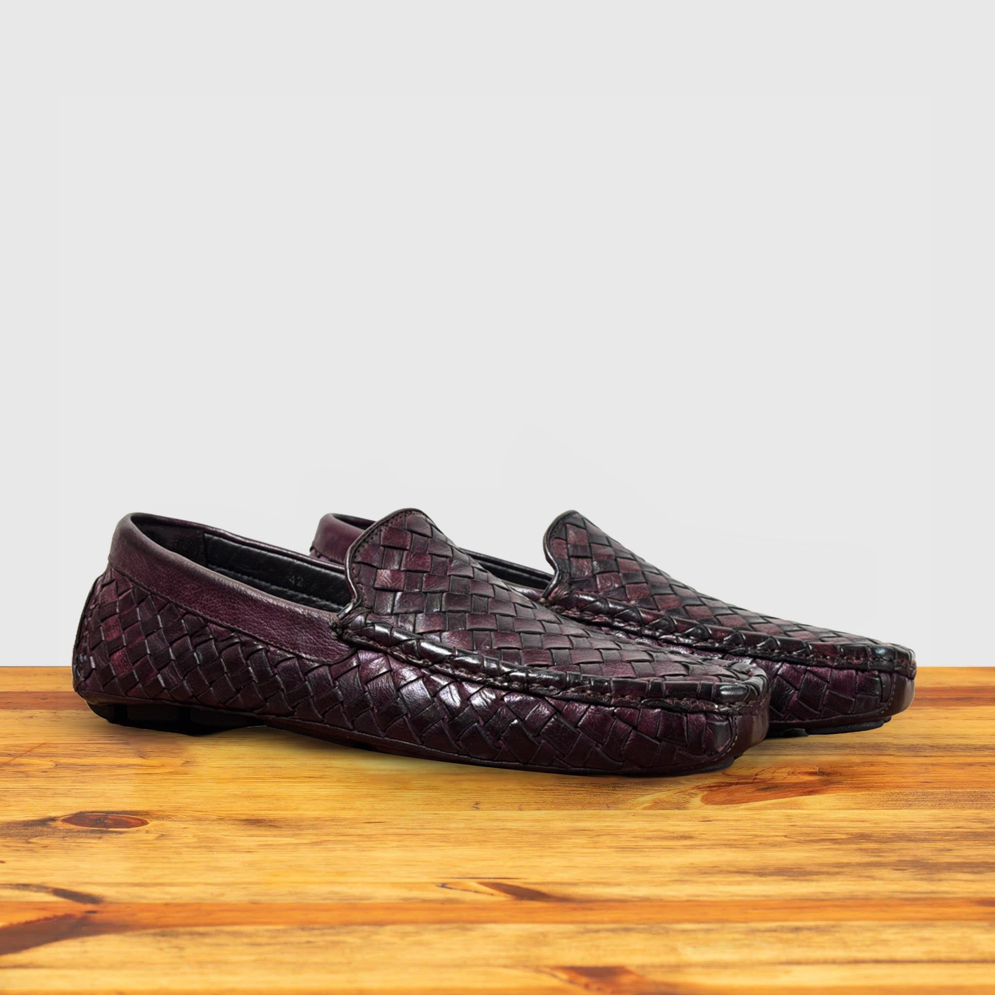 A Pair of Merlot loafer shoe with woven pattern on a wooden surface