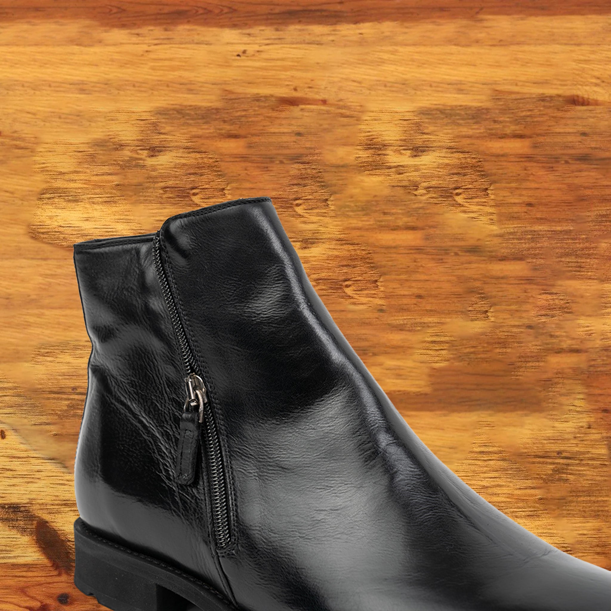 Black leather ankle boot with a zipper on a wooden surface