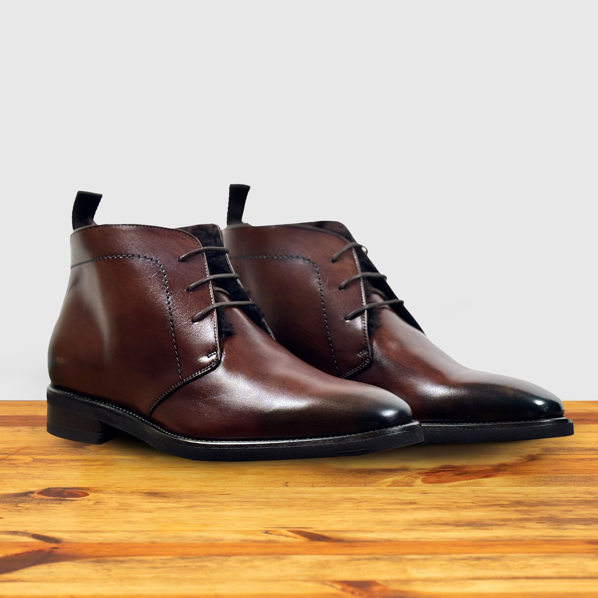 Pair of brown leather boots on a wooden surface with a light gray background