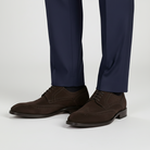 Brown dress shoes worn with navy blue pants on a light gray background