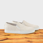 A Side view of White woven slip-on shoe on a wooden surface with a white background