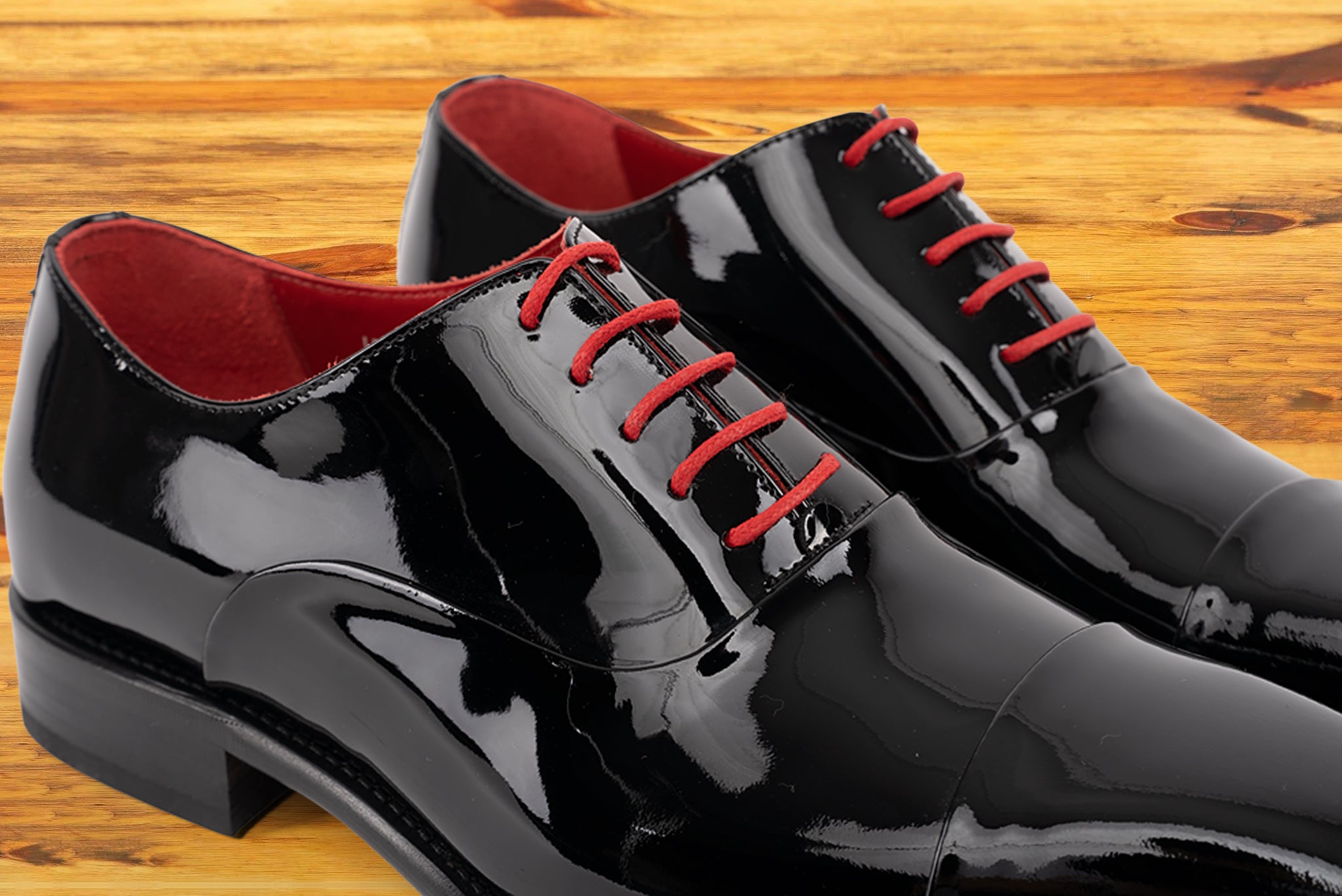Pair of Black patent leather shoe with red laces on a wooden surface