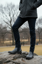 Person wearing a dark jacket, black pants, and Pair of Stone leather Chelsea boots standing on a rock in a park.