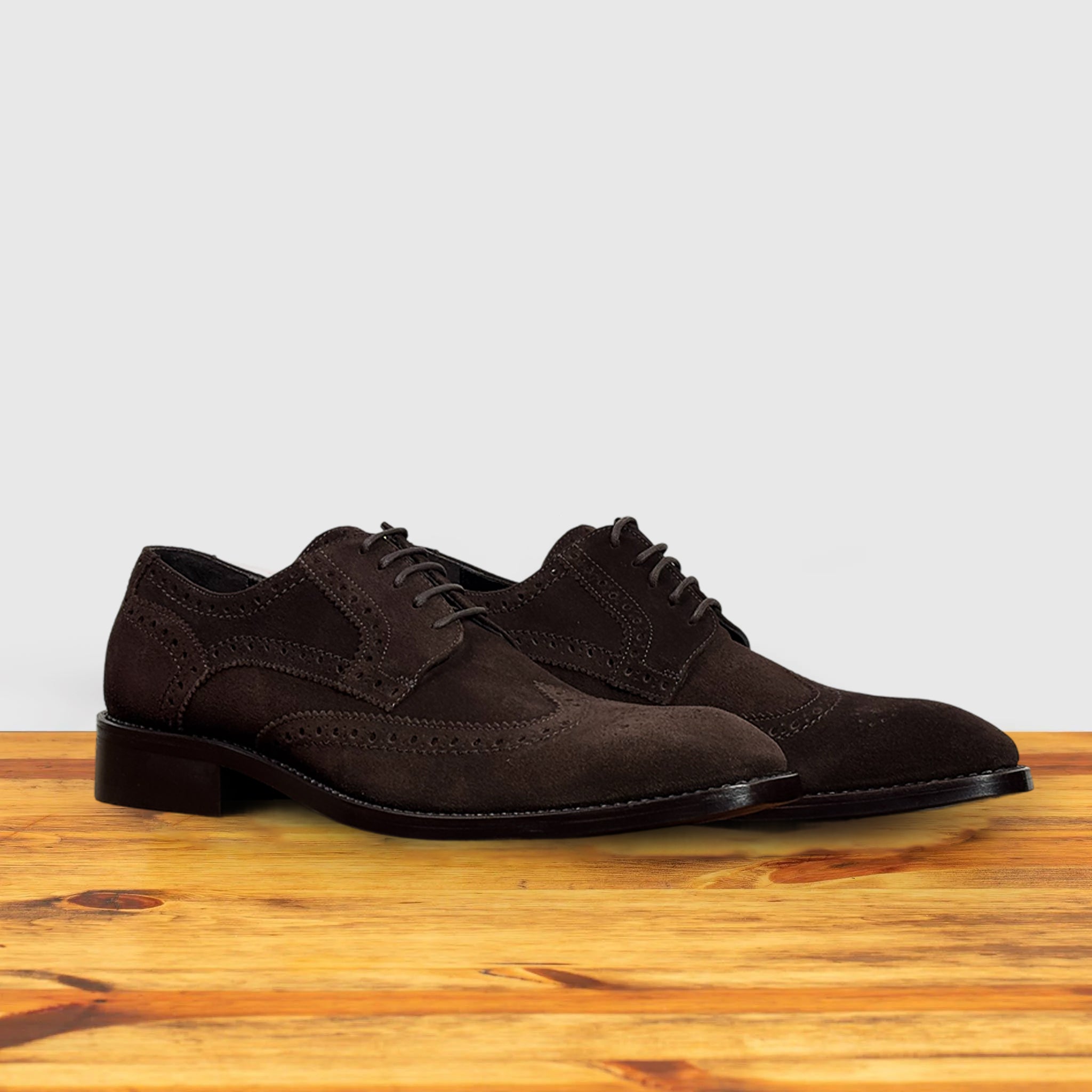 Pair of Brown suede dress shoe on a wooden surface with a light gray background