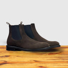 A pair of Brown suede Chelsea boot on a wooden surface with a light gray background