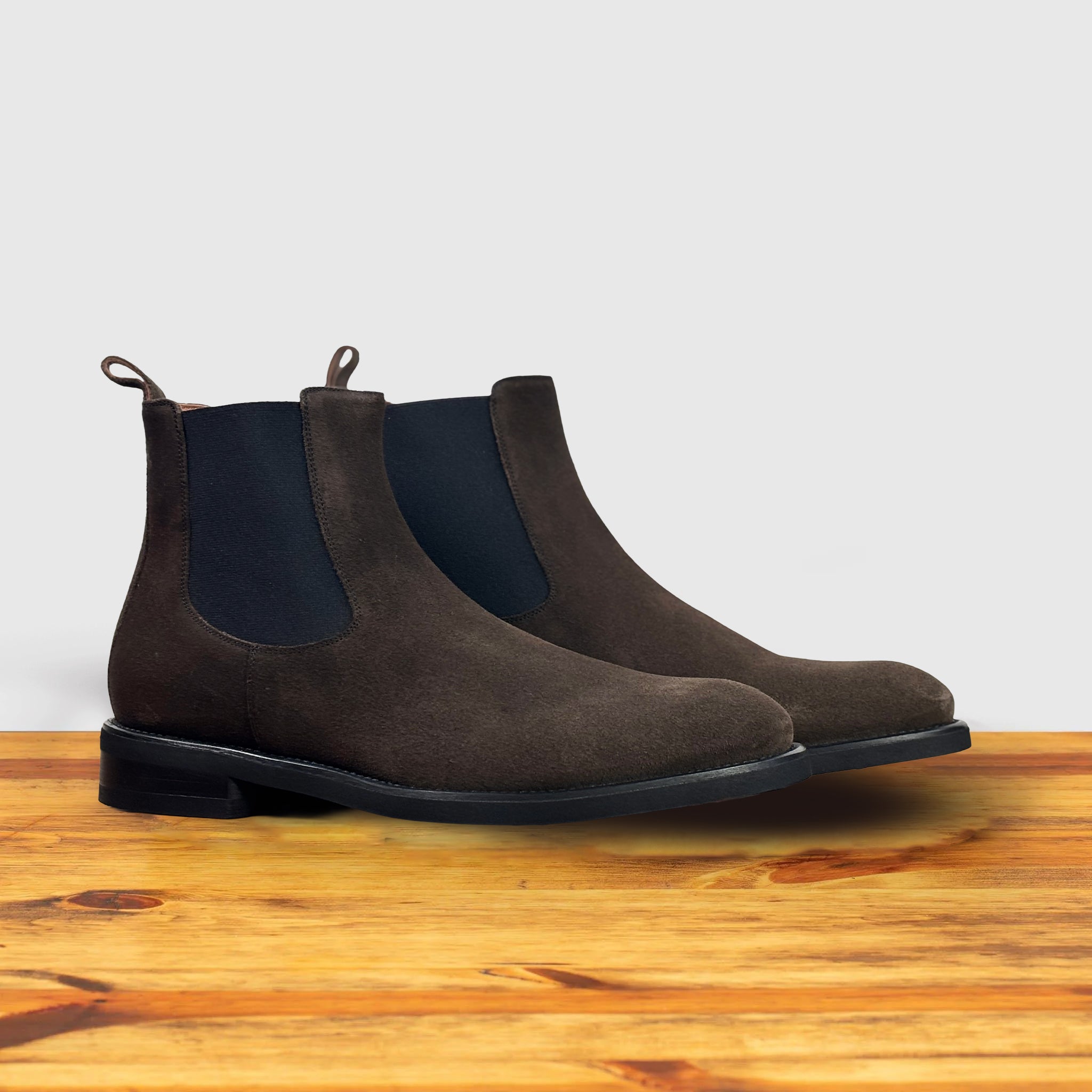 A pair of Brown suede Chelsea boot on a wooden surface with a light gray background
