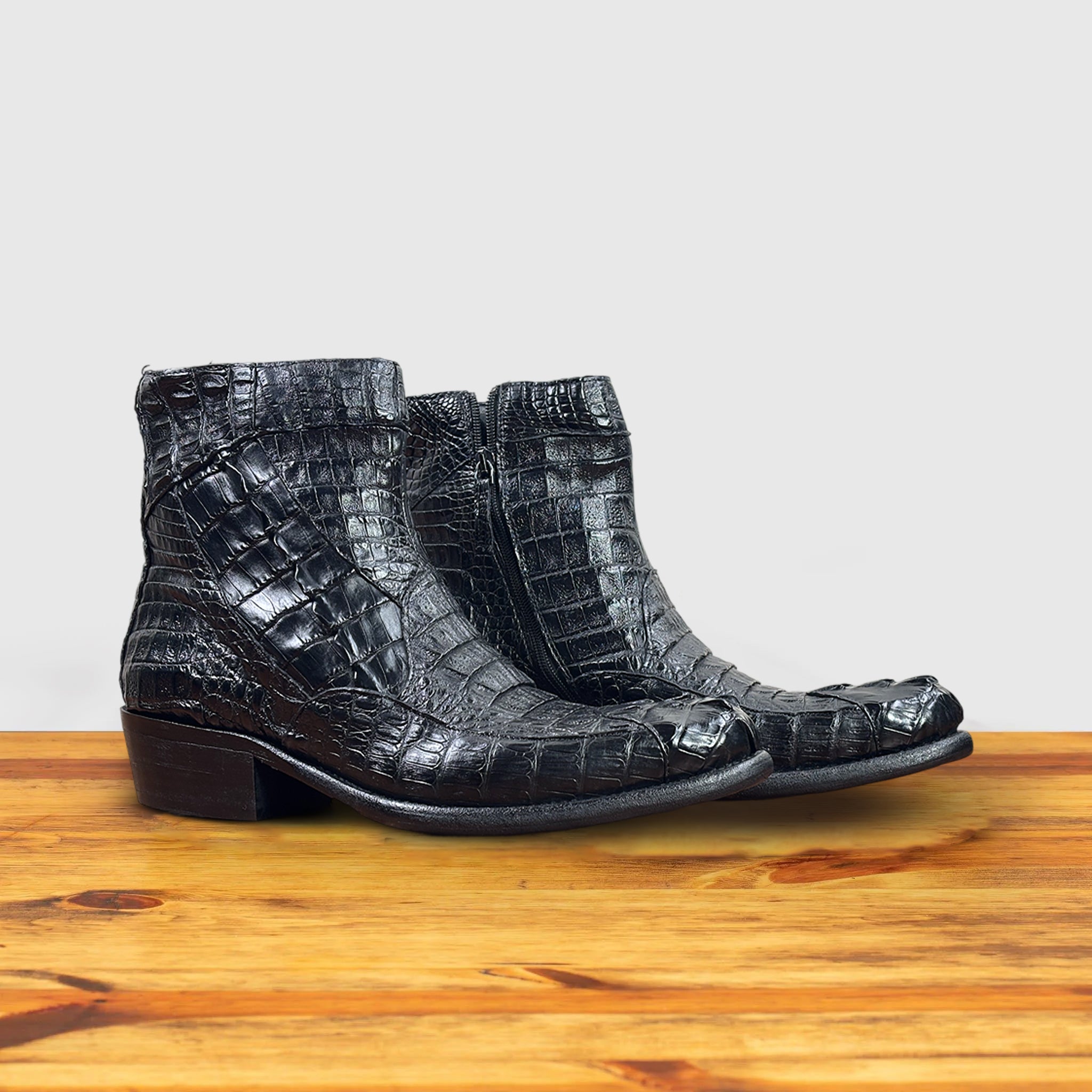 Pair of Black crocodile western boot on a wooden surface with a light gray background