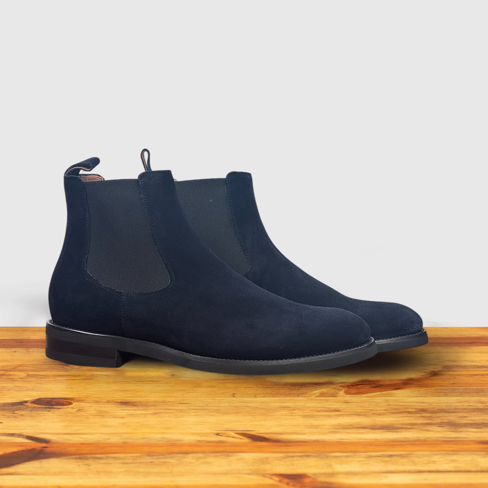 Pair of Navy blue Chelsea boot on a wooden surface with a light gray background