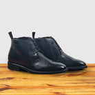 A pair of Black leather boot on a wooden surface with a light gray background
