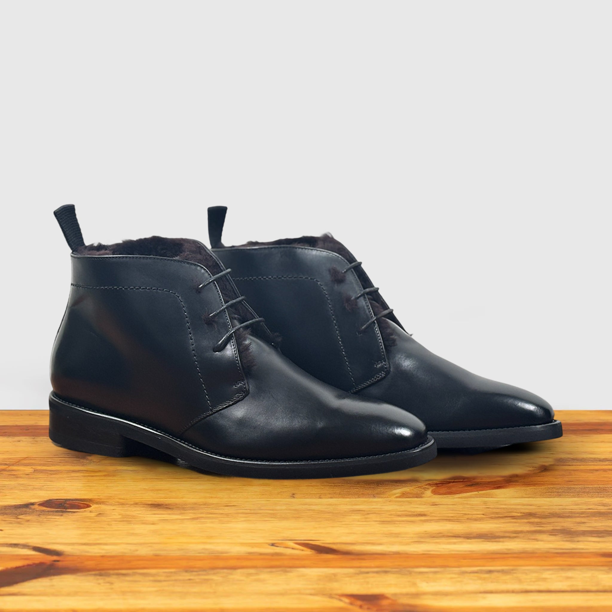 A pair of Black leather boot on a wooden surface with a light gray background