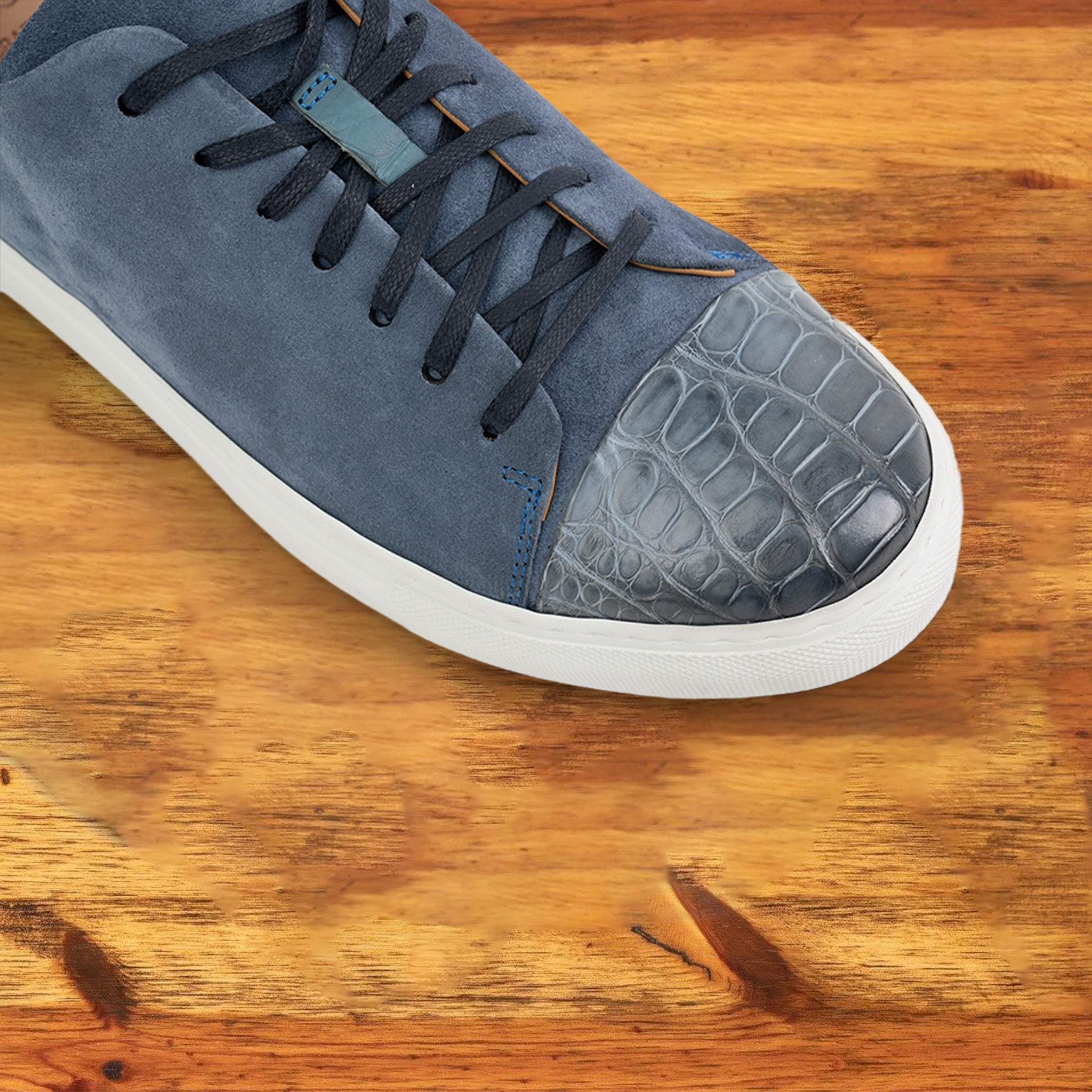 Blue suede sneaker with white sole on a wooden surface
