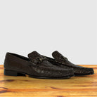 A pair of dark brown textured leather loafers, displayed on a wooden surface against a light gray background.
