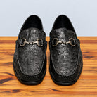 Pair of Black ostrich loafers on top of a wooden surface
