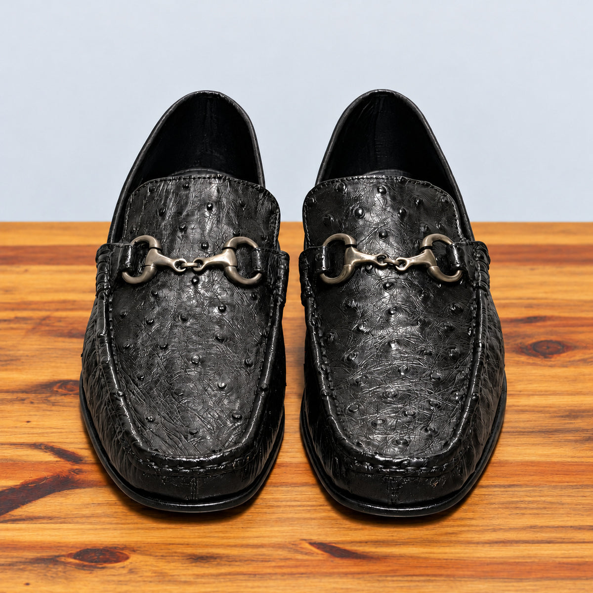 Pair of Black ostrich loafers on top of a wooden surface