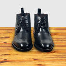 A pair of Black leather boot on a wooden surface with a light gray background