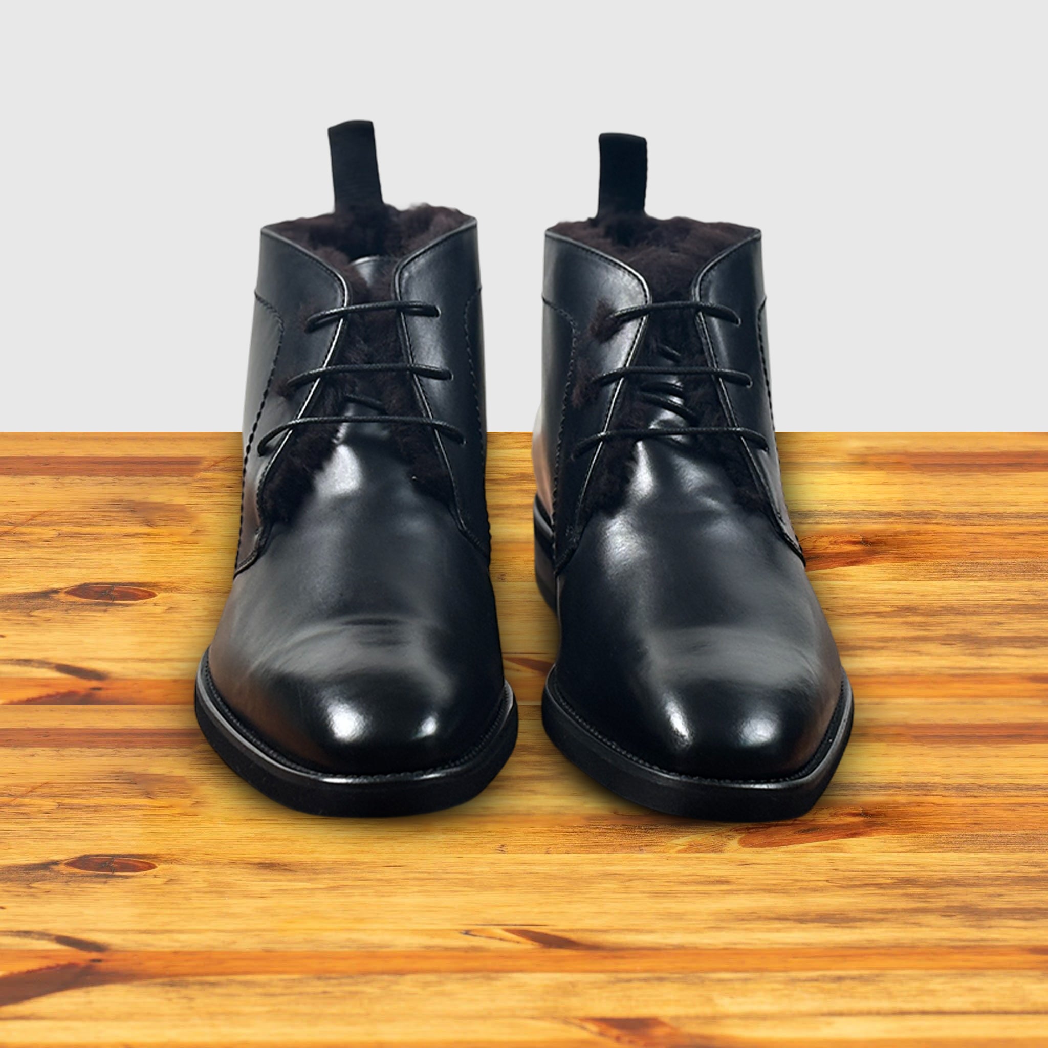 A pair of Black leather boot on a wooden surface with a light gray background