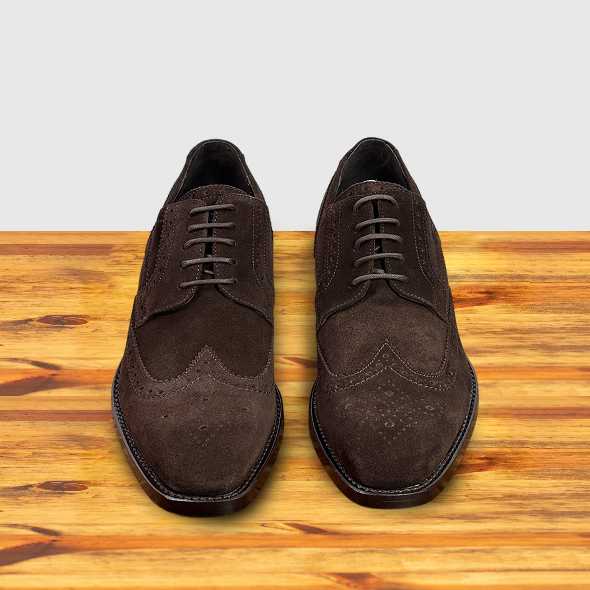 Pair of Brown suede dress shoe on a wooden surface with a light gray background