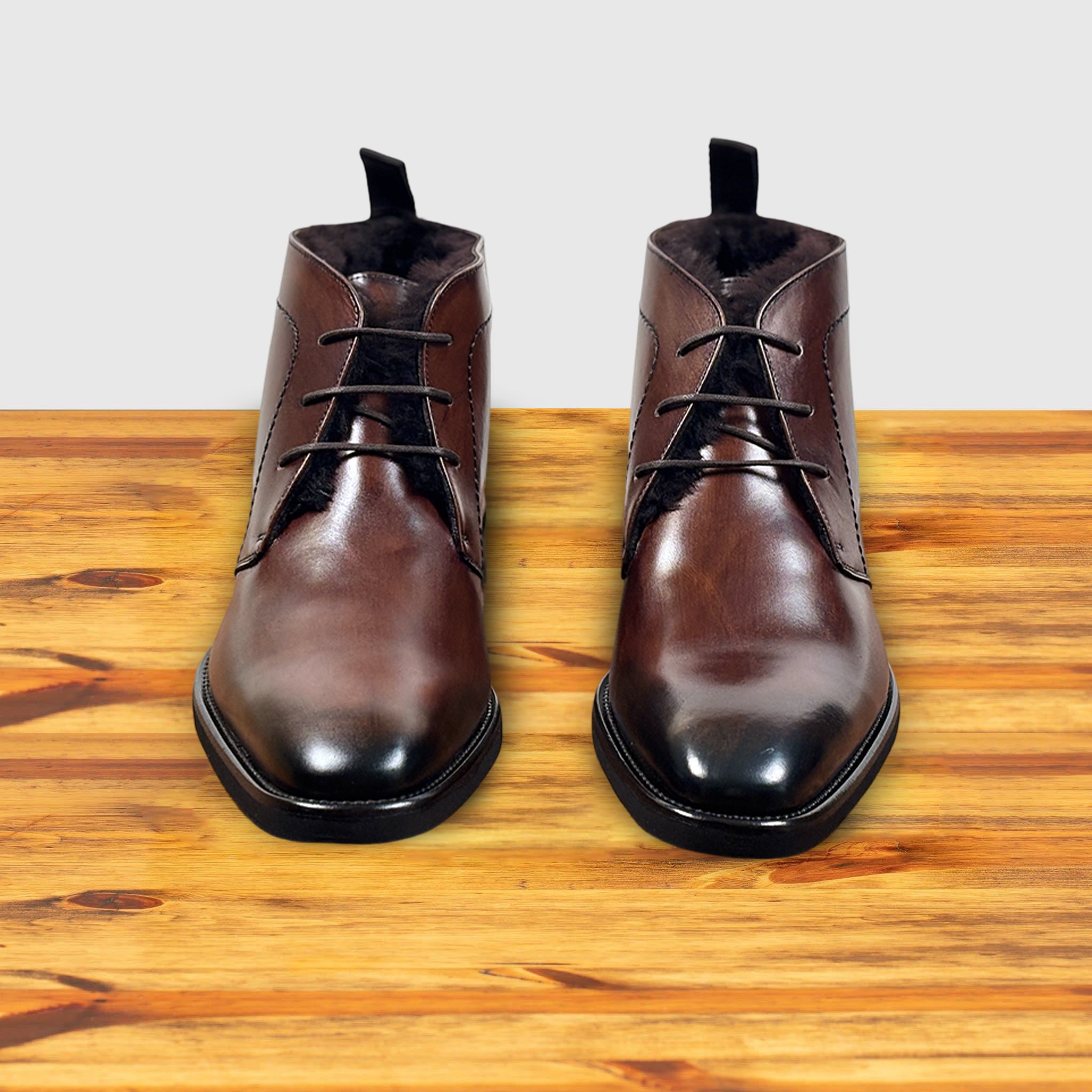 Pair of brown leather boots on a wooden surface with a light gray background