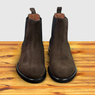 A pair of Brown suede Chelsea boot on a wooden surface with a light gray background
