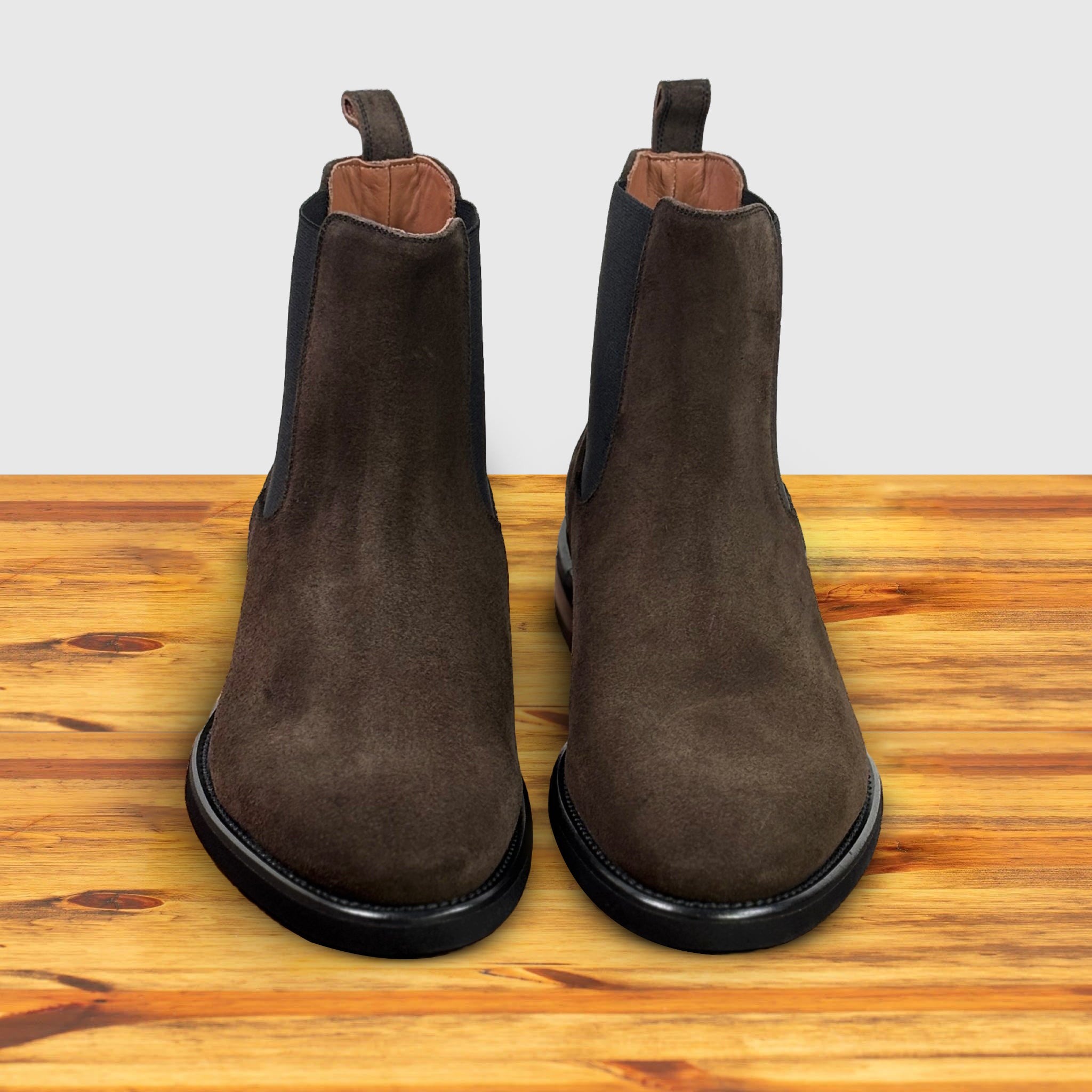 A pair of Brown suede Chelsea boot on a wooden surface with a light gray background