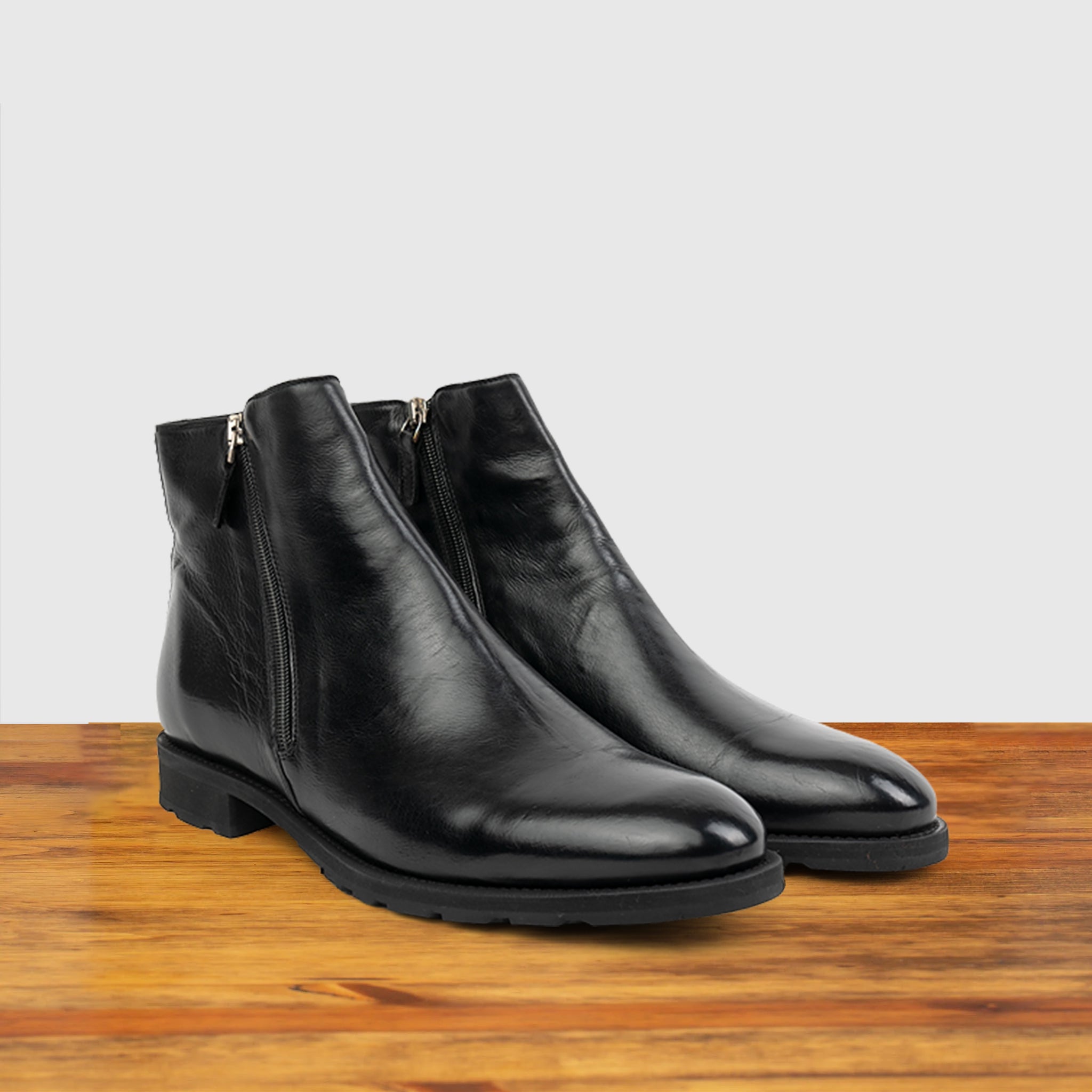 A Pair of Black leather ankle boot with a zipper on a wooden surface