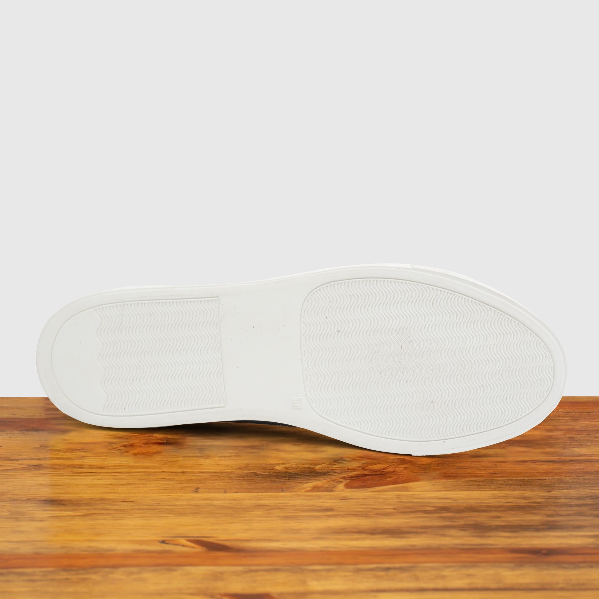 Outsole of Blue suede sneaker with white sole on a wooden surface