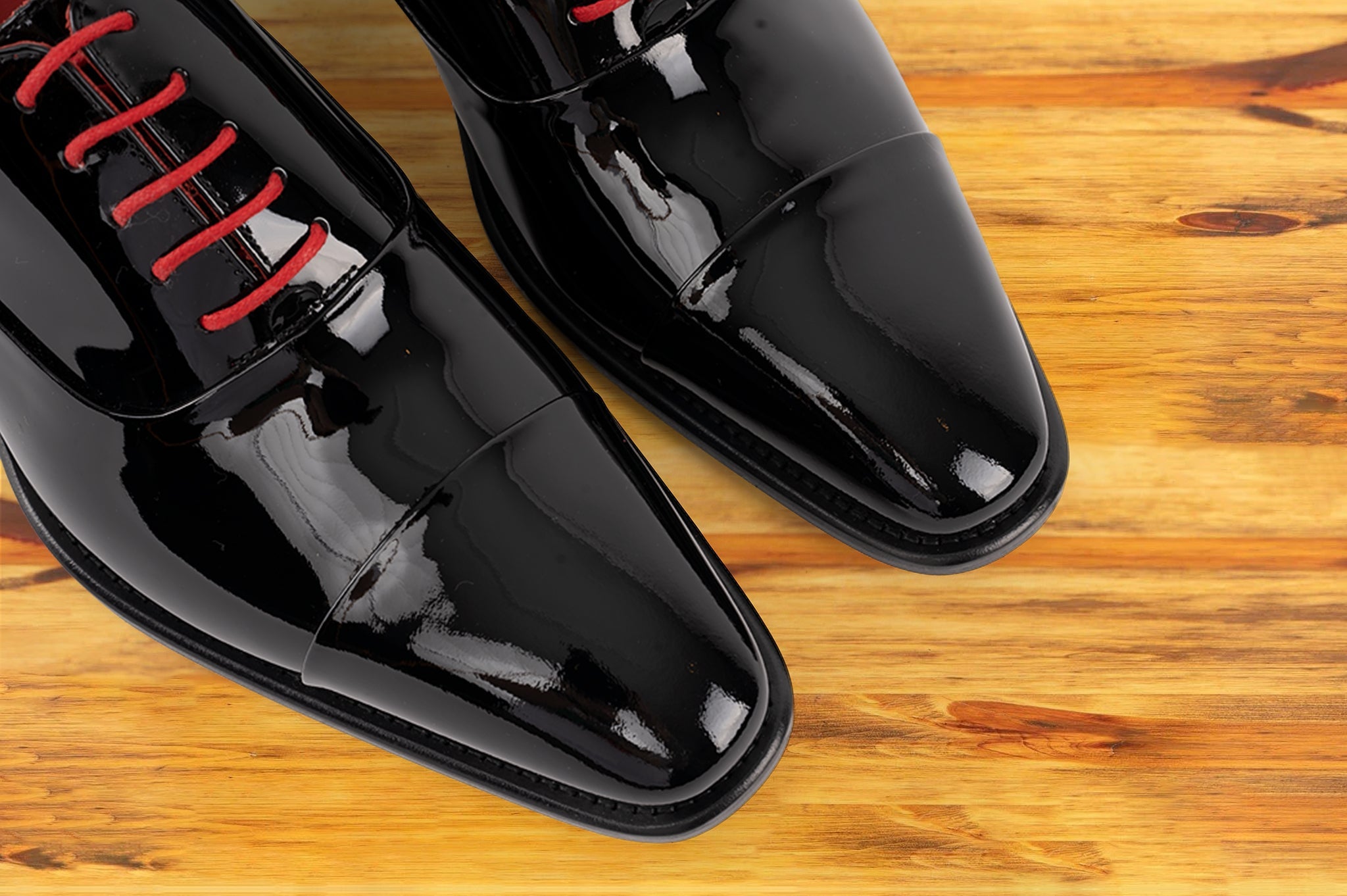 Pair of Black patent leather shoe with red laces on a wooden surface