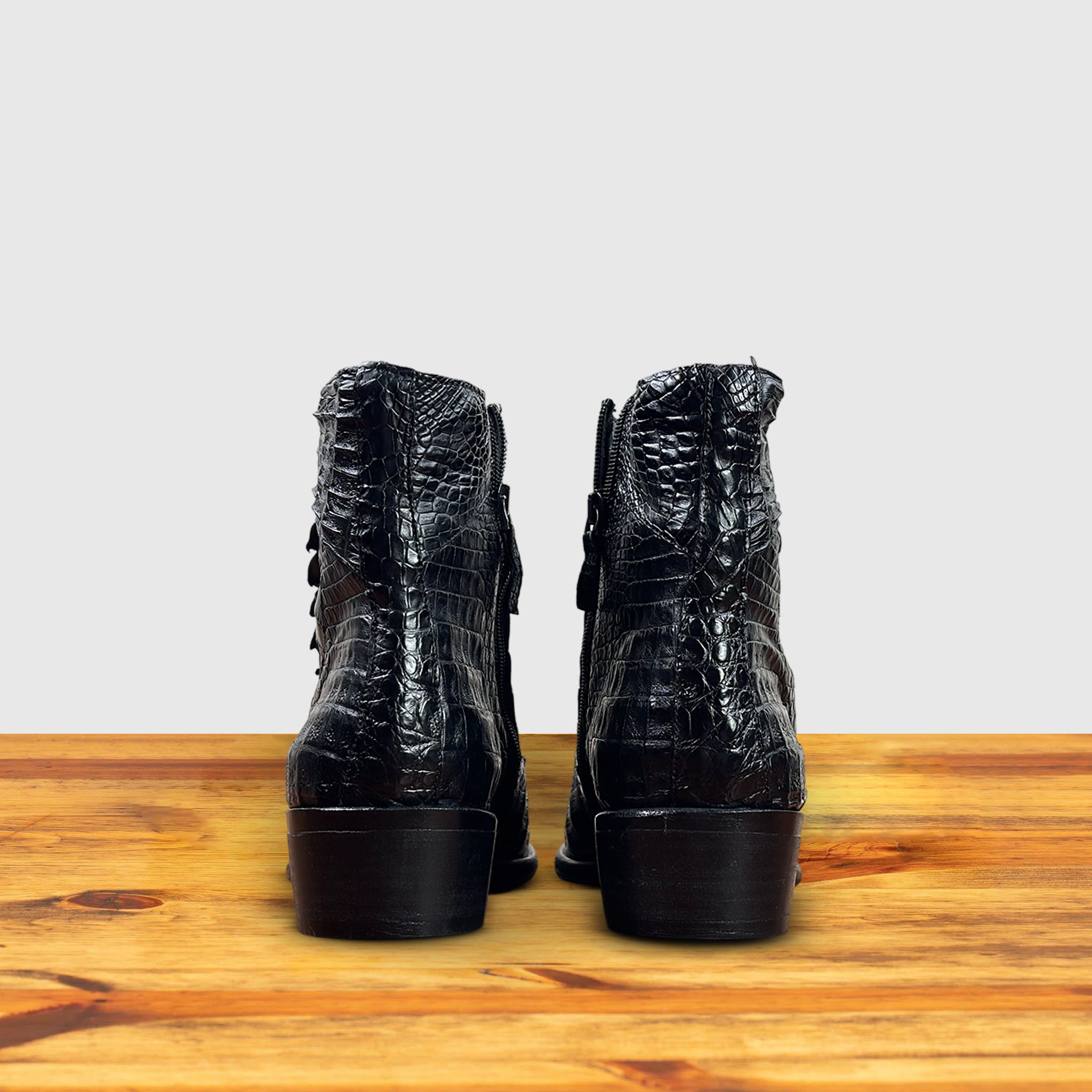 Pair of Black crocodile western boot on a wooden surface with a light gray background