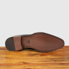 Outsole of Black wholecut dress shoe on a wooden surface with a light gray background