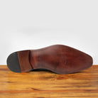 Outsole of Black leather dress shoe on a wooden surface with a gray background