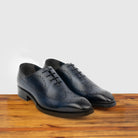 A Pair of Blue wholecut dress shoe on a wooden surface with a light gray background