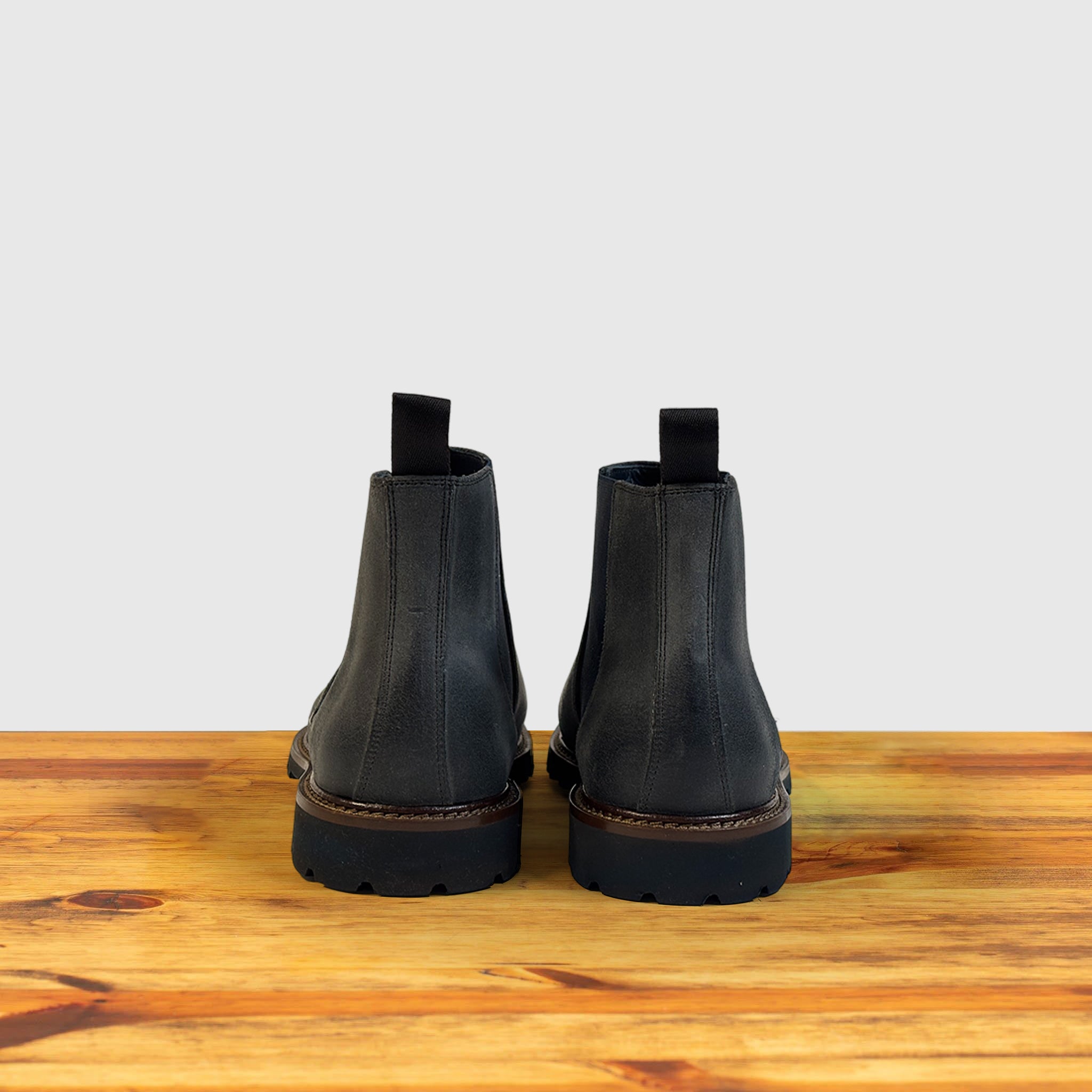 Pair of Stone leather Chelsea boots on a wooden surface with a light gray background