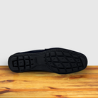 Outsole of a navy blue suede penny loafer with a  strap, displayed on a wooden surface.